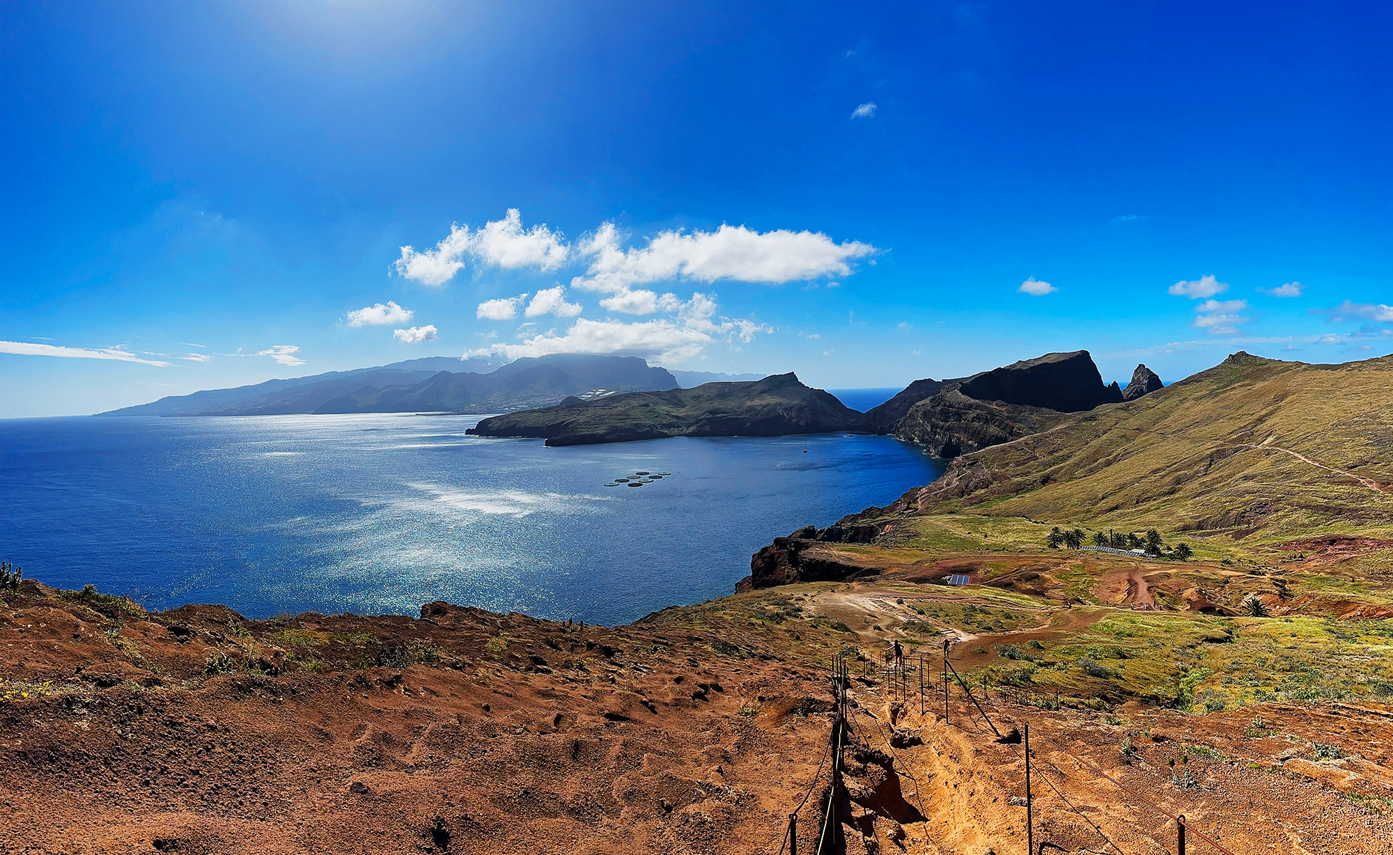 Panoramic view of PR8 Vereda da Ponta de S. Lourenço trail with rugged cliffs, blue ocean, and distant mountains.